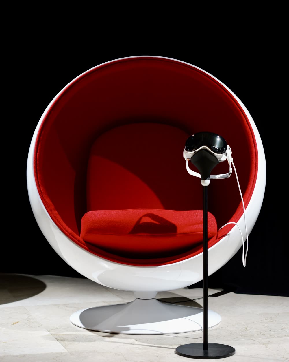 An Apple Vision Pro on a stand beside a red ball chair in the exhibition